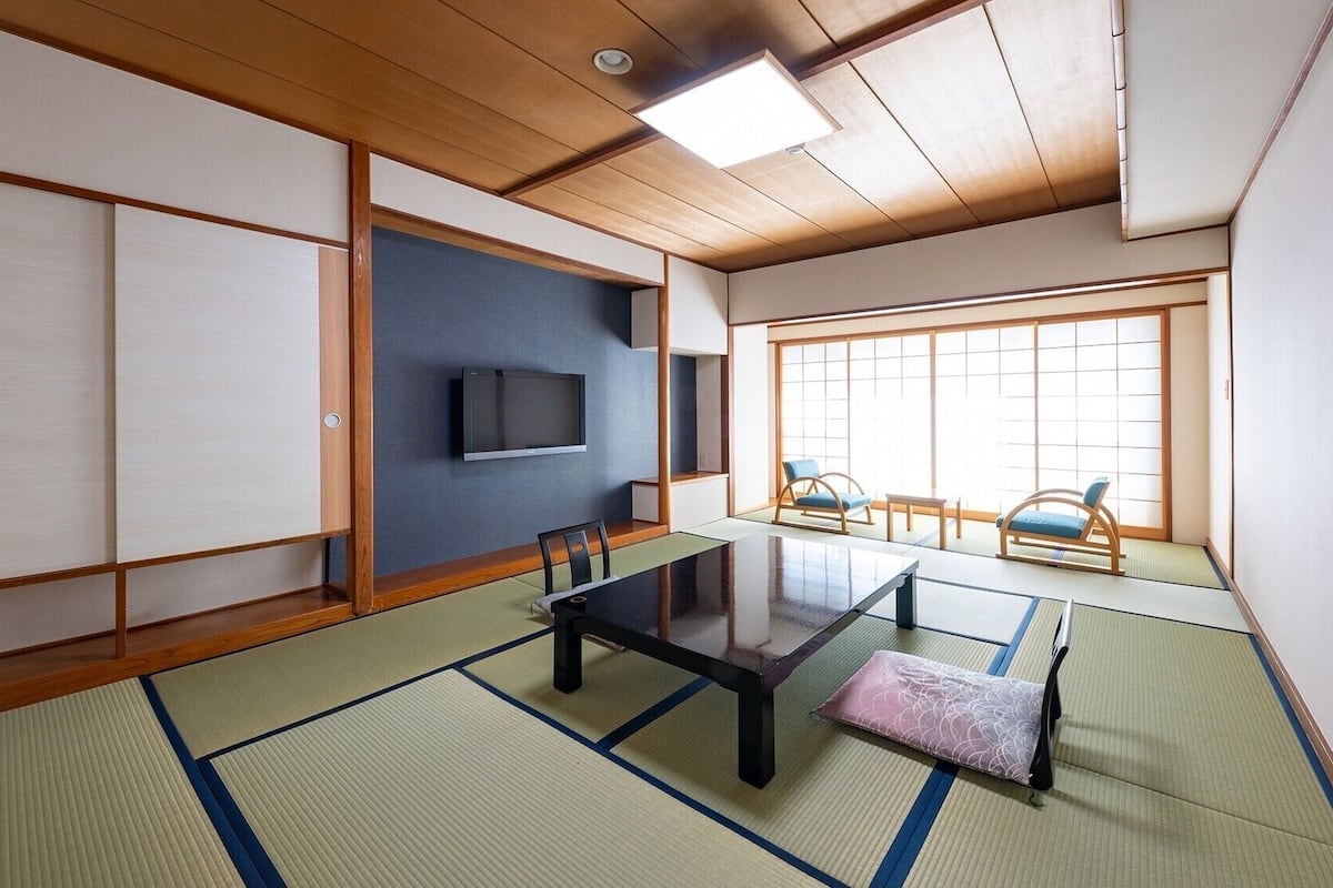 A traditional Japanese room with tatami flooring, a low table, a TV, and sliding doors.