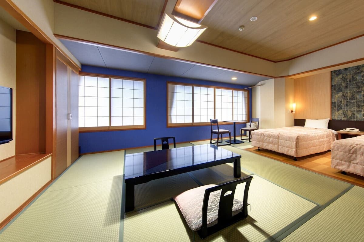 A traditional Japanese-style room with tatami flooring, a low table, two beds, and a large window.