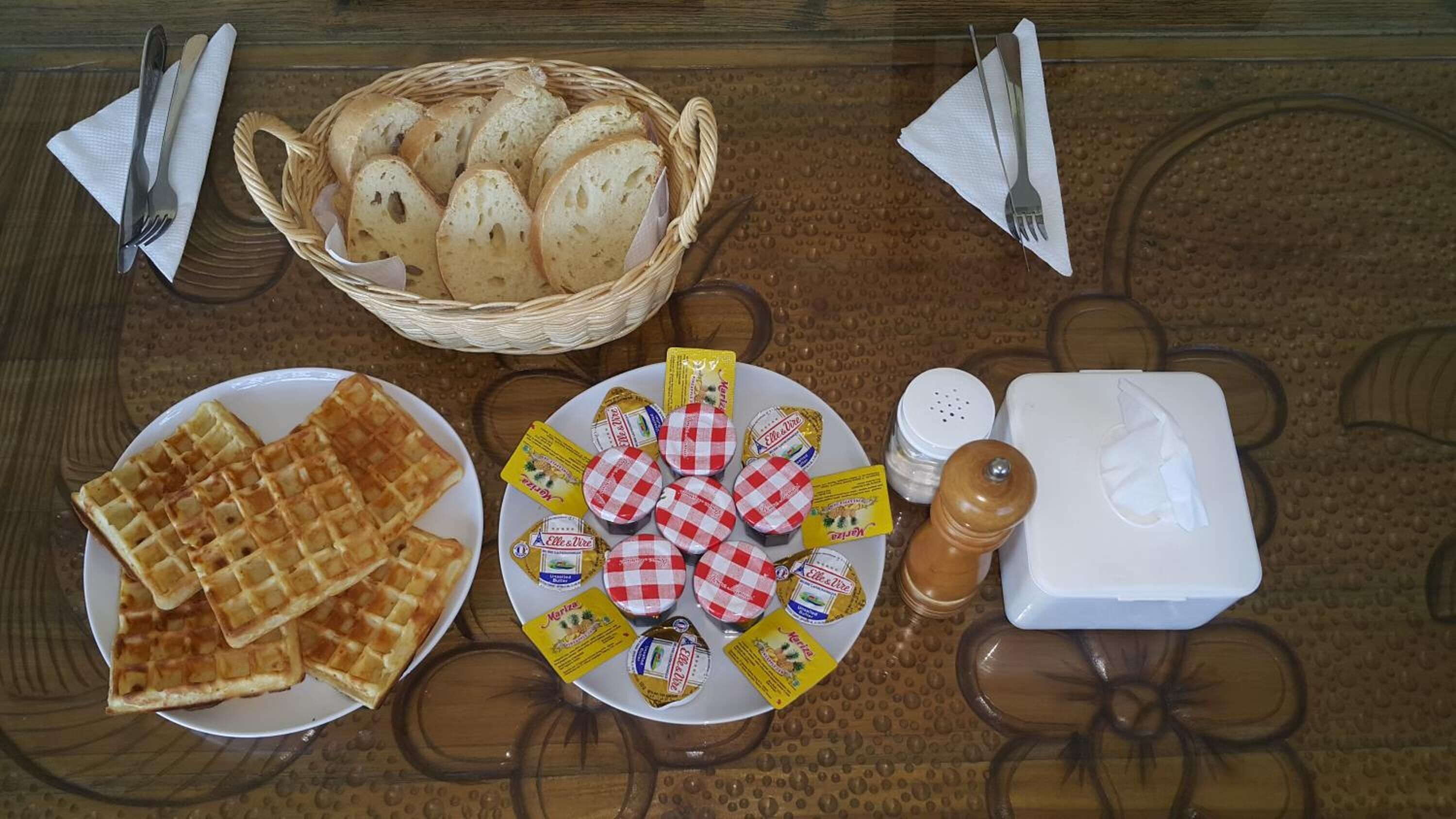Pöydällä on leipäkori, lautasellinen vohveleita ja juustoa sekä erilaisia lisukkeita.