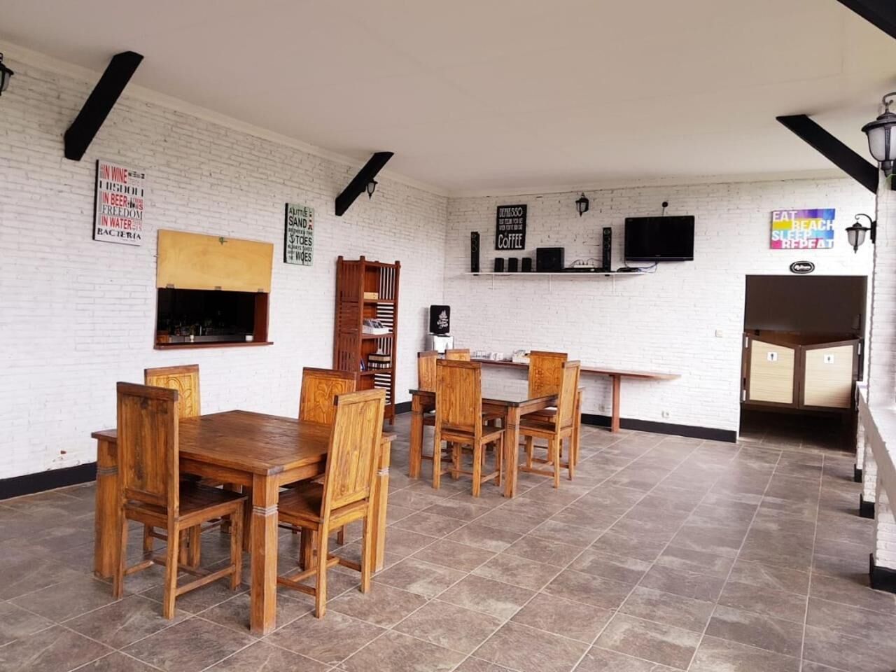 A dining area with wooden tables and chairs, a white brick wall, and a flat-screen TV mounted above a counter.
