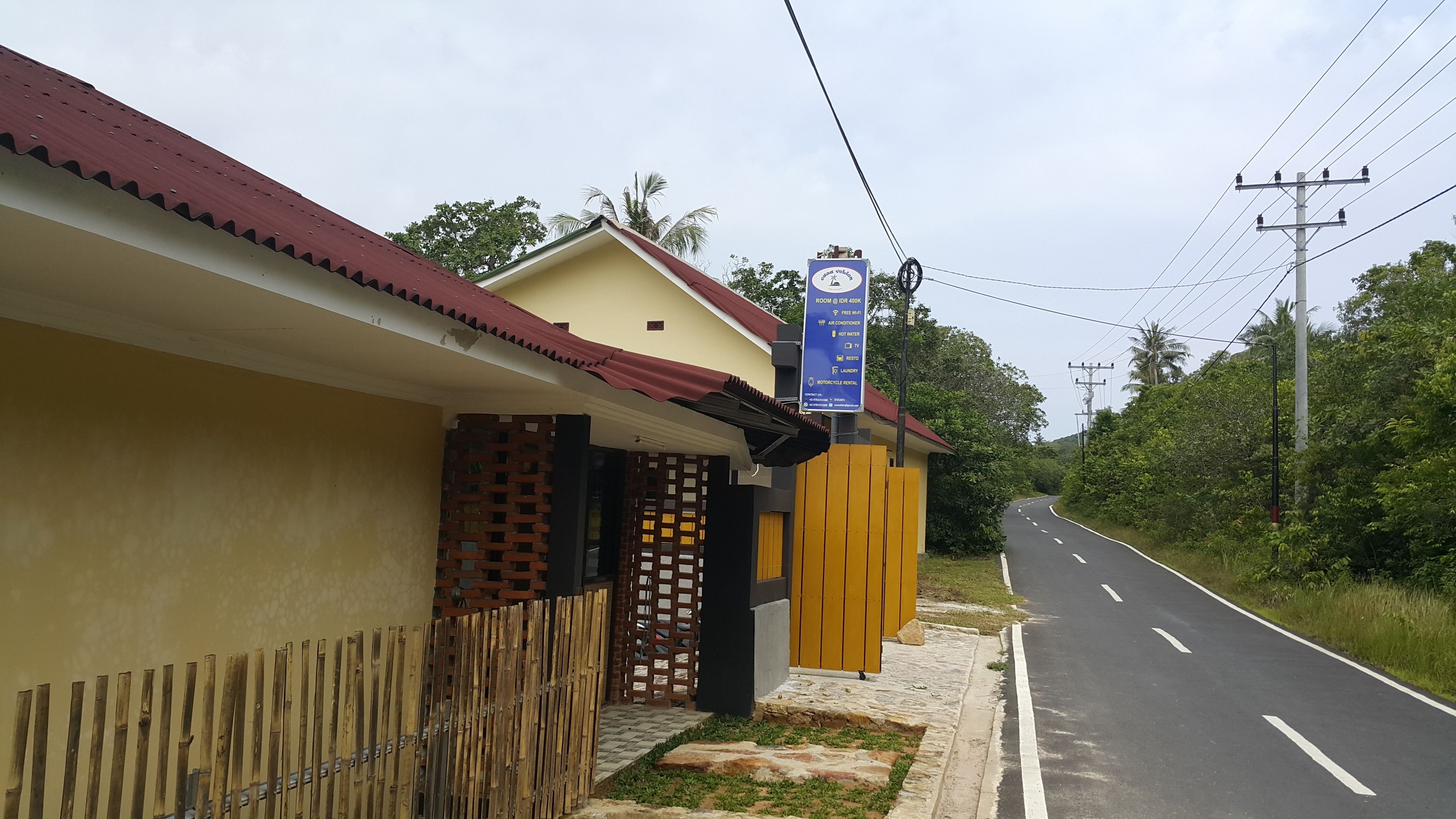 A roadside hotel with a signboard listing amenities like free Wi-Fi, air conditioning, hot water, and laundry services.