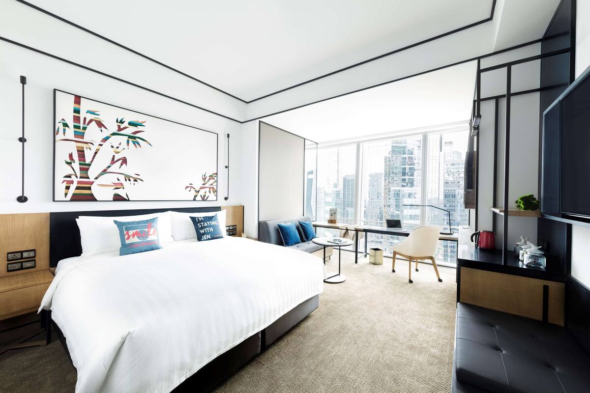 Une chambre d’hôtel moderne avec un grand lit, un canapé, une petite table et un téléviseur.