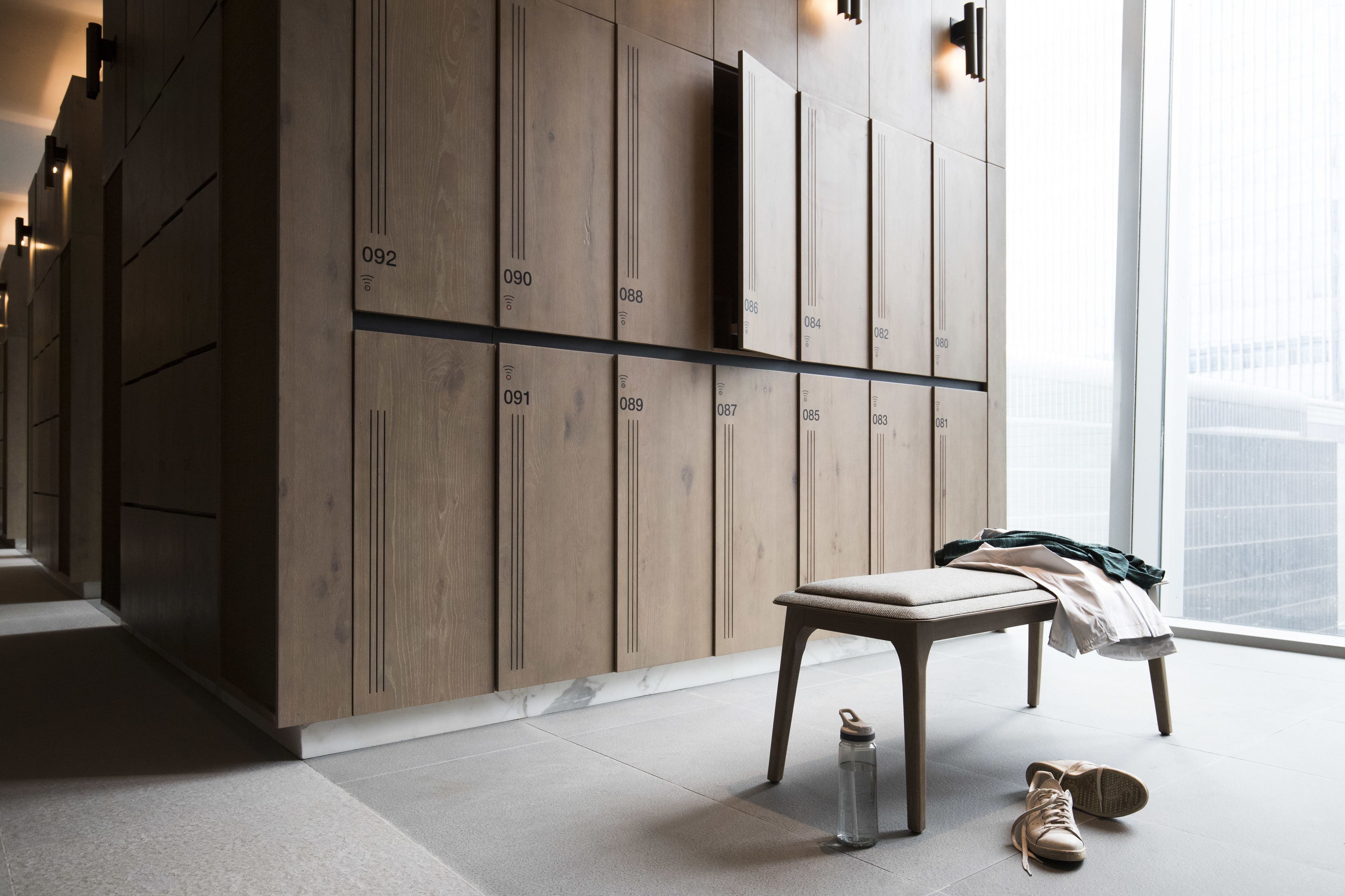 A modern hotel room with a large wardrobe, a bench, a water bottle, and a pair of shoes on the floor.