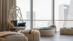 A modern interior with a hanging chair, ottomans, and a view of a cityscape through large windows.