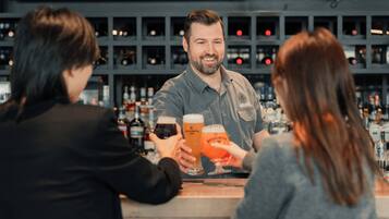 A bar setting with a bartender and two customers holding glasses of beer.