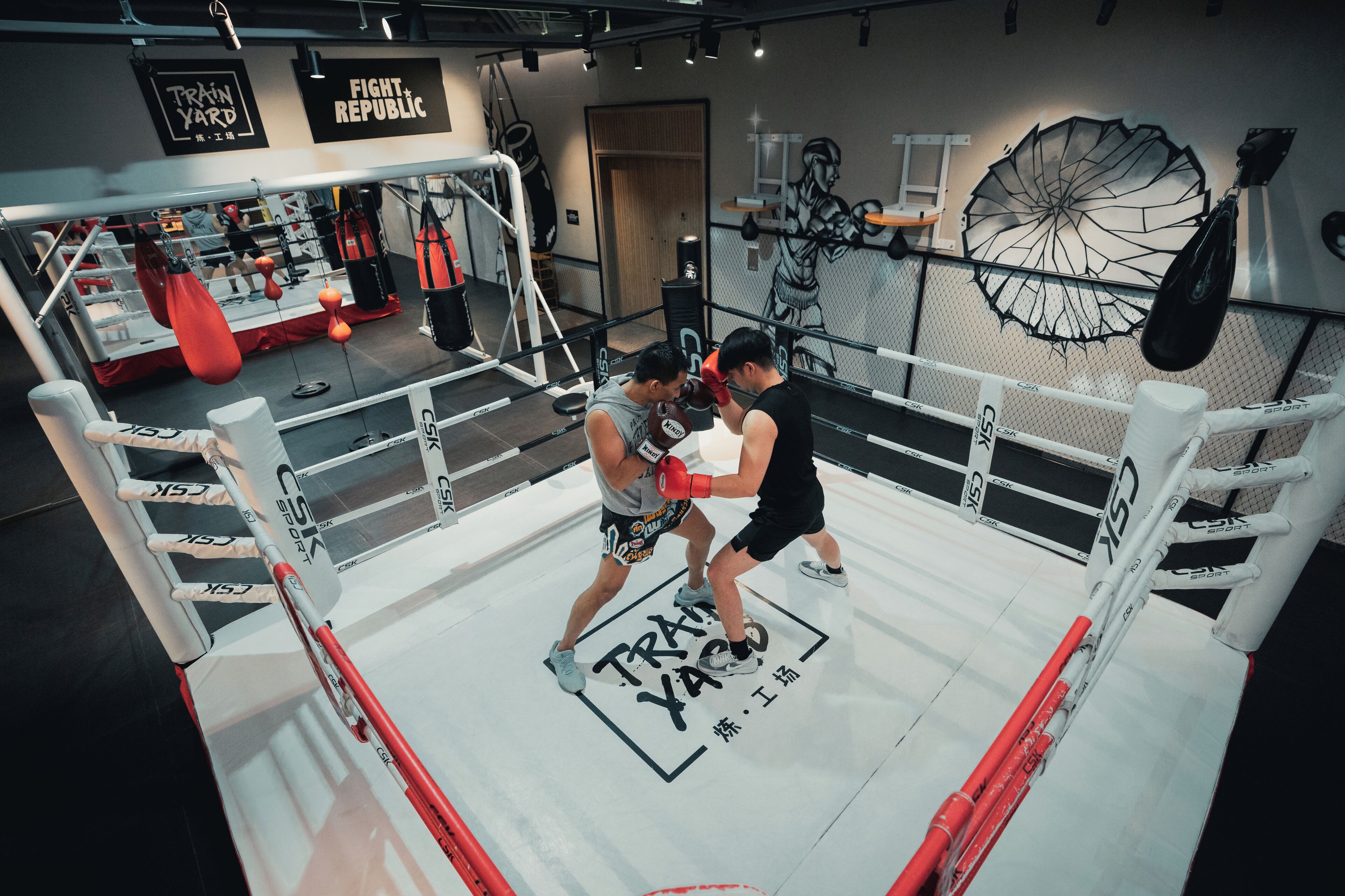 A boxing ring with "TRAIN YACCO" branding, surrounded by boxing equipment and a punching bag.