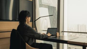 A person working at a desk with a laptop, large windows, and a view of a cityscape.
