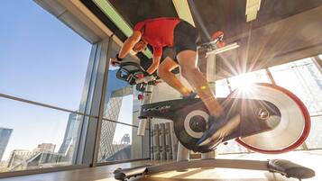 A person using a stationary bike in a gym with large windows and a city view.