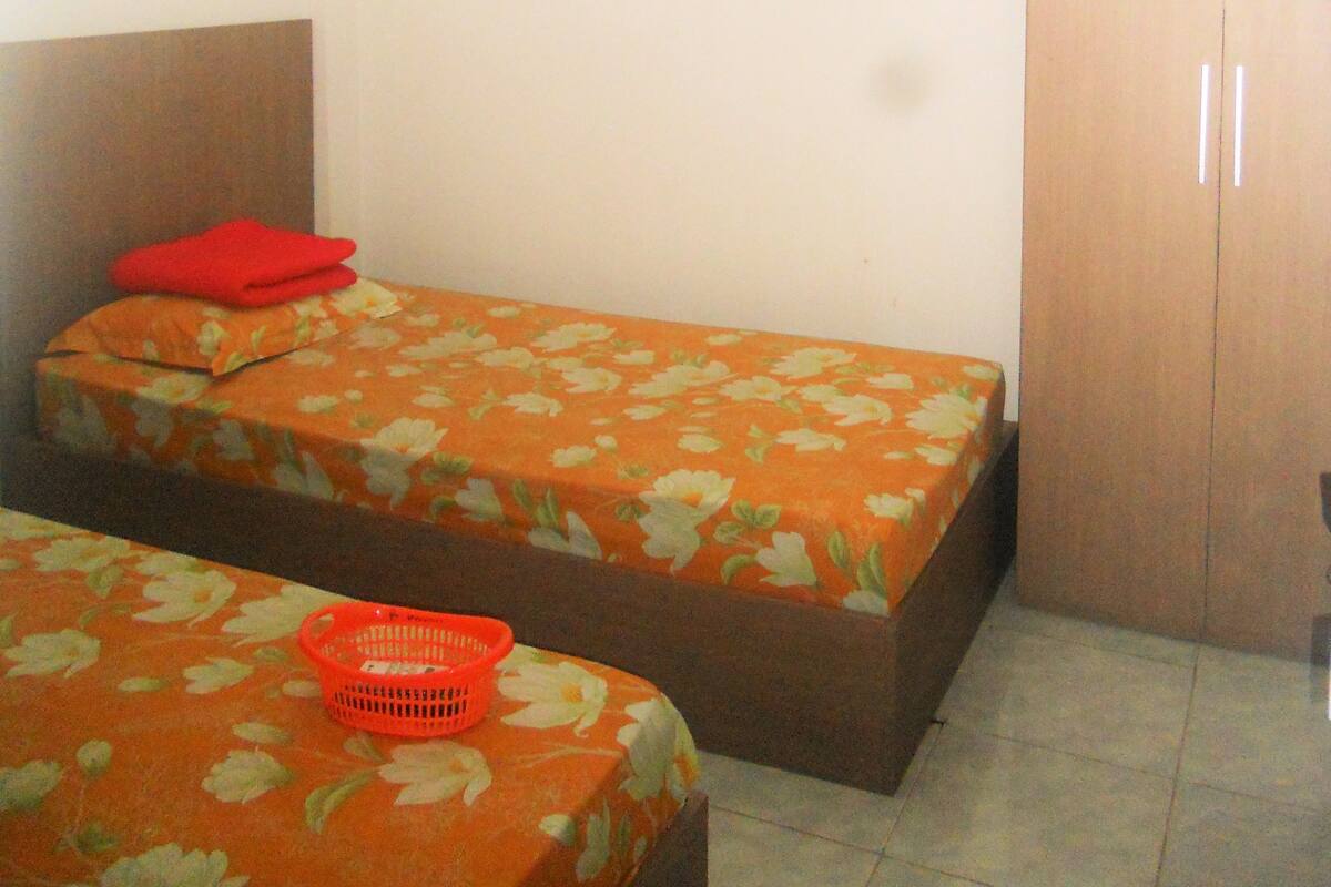 A small room with two single beds, a wooden wardrobe, and a wall-mounted air conditioner.