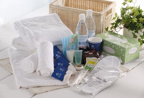 A neatly arranged set of toiletries and towels on a white surface, including a wicker basket, bottled water, and a potted plant.