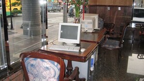 A computer desk with a monitor, keyboard, and mouse in a room with a patterned chair and a large window. - Noble Hotel (Kaohsiung)