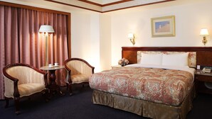 A hotel room with a large bed, two chairs, a small table, and a nightstand with a lamp. - Noble Hotel (Kaohsiung)