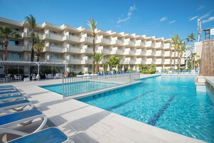 A hotel with a swimming pool, lounge chairs, and palm trees.