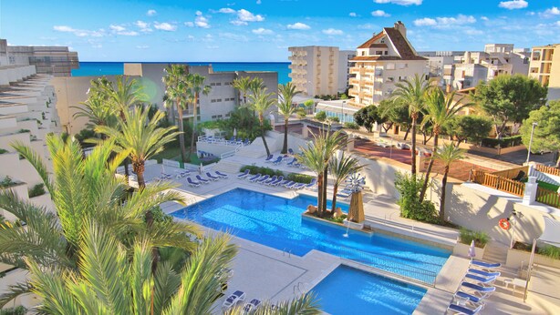 Um resort com uma piscina grande, espreguiçadeiras, palmeiras e vista para o oceano.