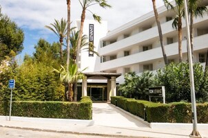 Una entrada de hotel moderna con fachada blanca, palmeras y un letrero que dice "SOM LIEVANT".