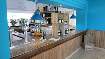 Uma área de bar com bancada de granito, prateleiras cheias de garrafas e estrutura de madeira.