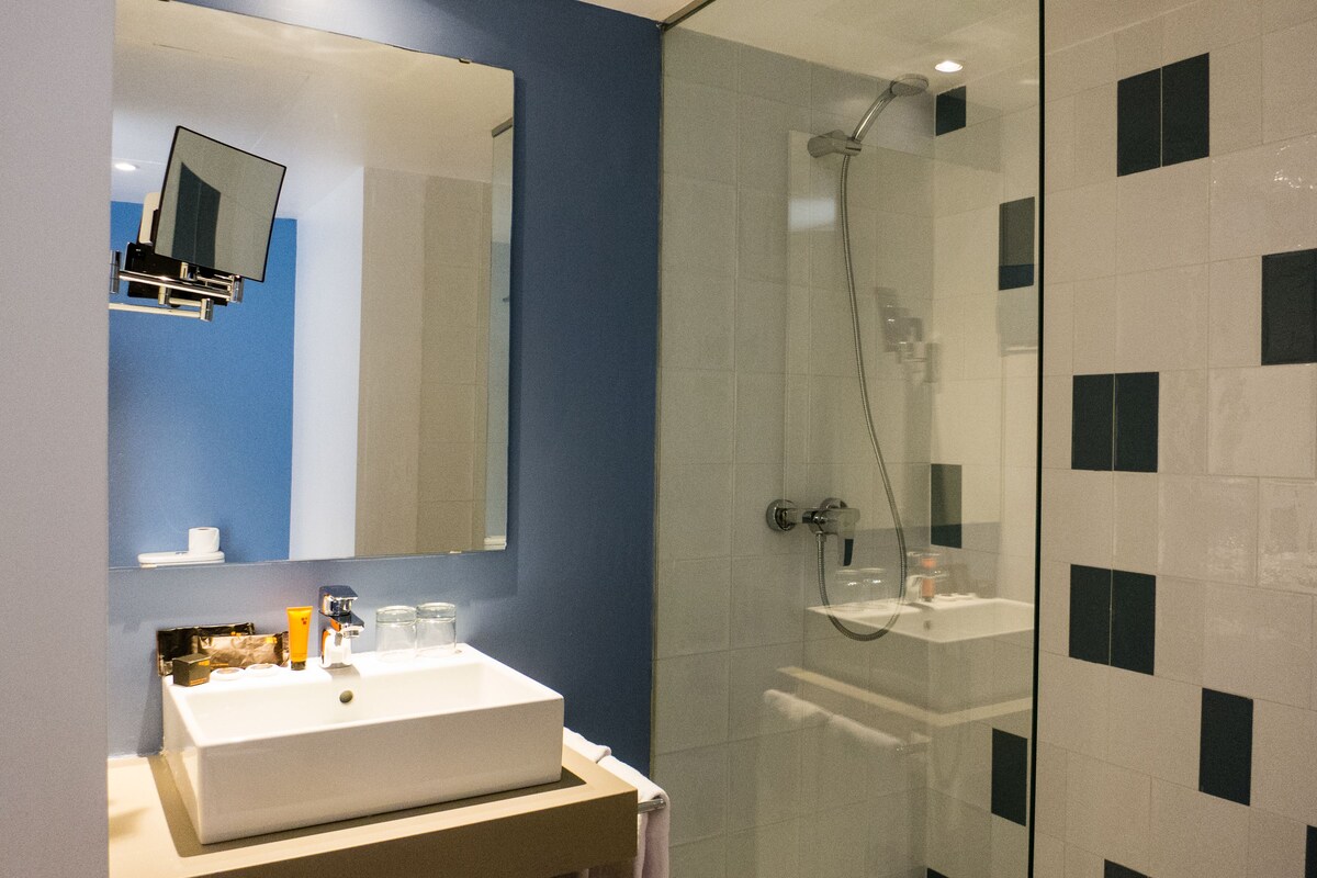 A modern bathroom with a glass-enclosed shower, a white sink, and a mirror above it.