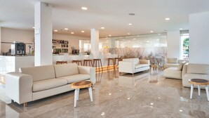 Uma sala de estar moderna com um sofá, poltronas e uma mesa de centro. Há também um espaço bar com banquetas e uma adega ao fundo.