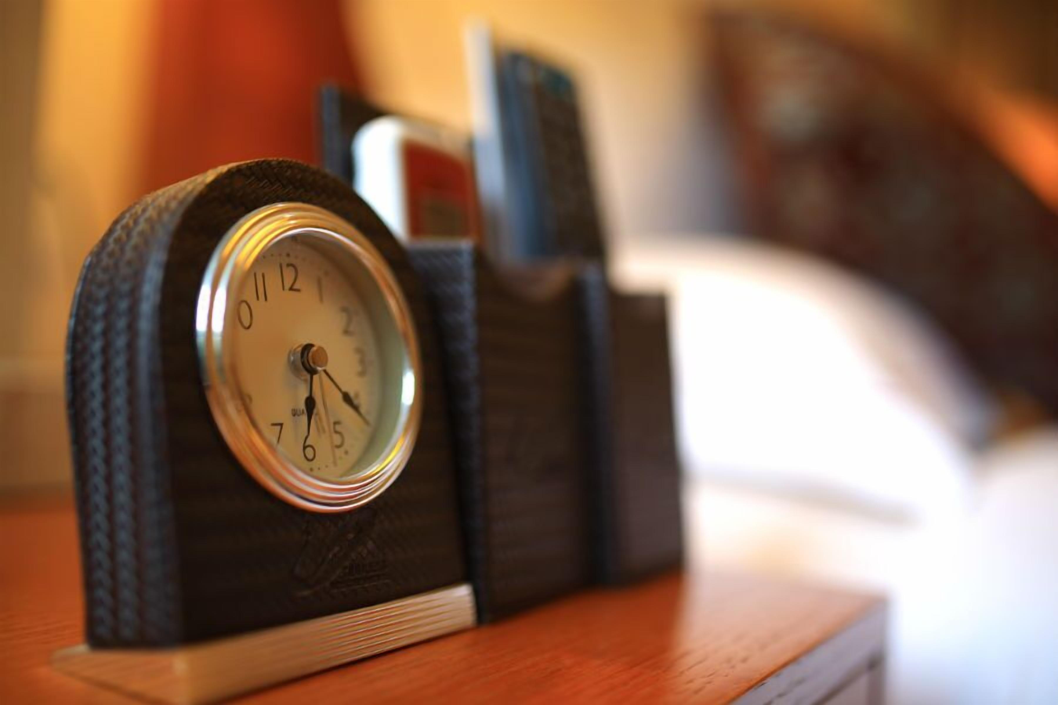 A clock with a dark, textured base and a white face, placed on a wooden surface.