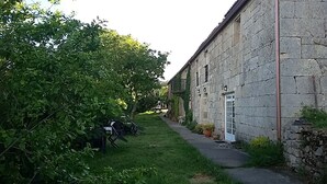 Un edificio de piedra estrecho con puerta y ventanas, rodeado de follaje y un sendero empedrado.
