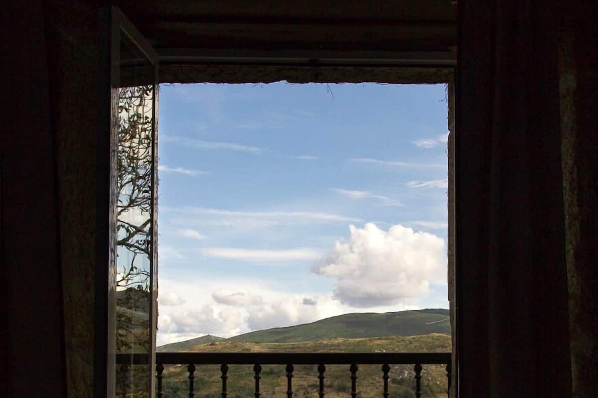 A room with a bed and a view of a mountainous landscape through a balcony.