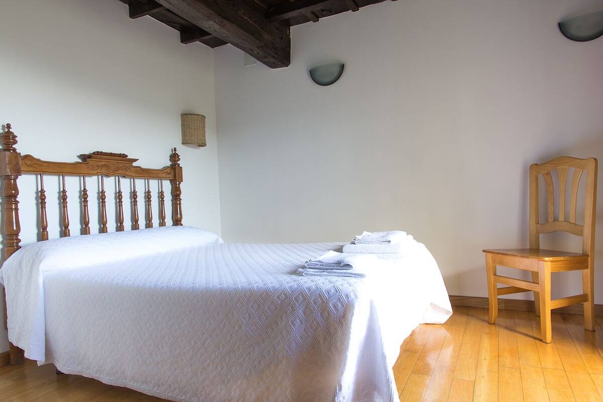 A bedroom with a wooden bed, a wooden chair, and a white bedspread.