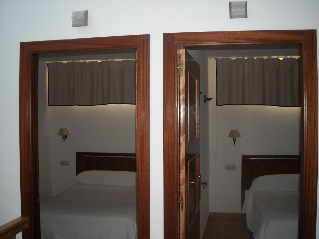 Dos dormitorios idénticos con cabeceras de madera, cada uno con una cama, una mesita de noche y una lámpara de pared.