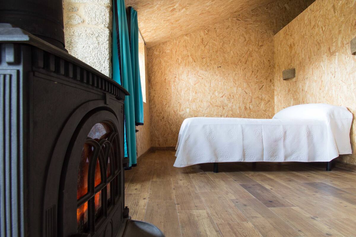 A room with a wooden floor, a bed with white bedding, a fireplace, and teal curtains.