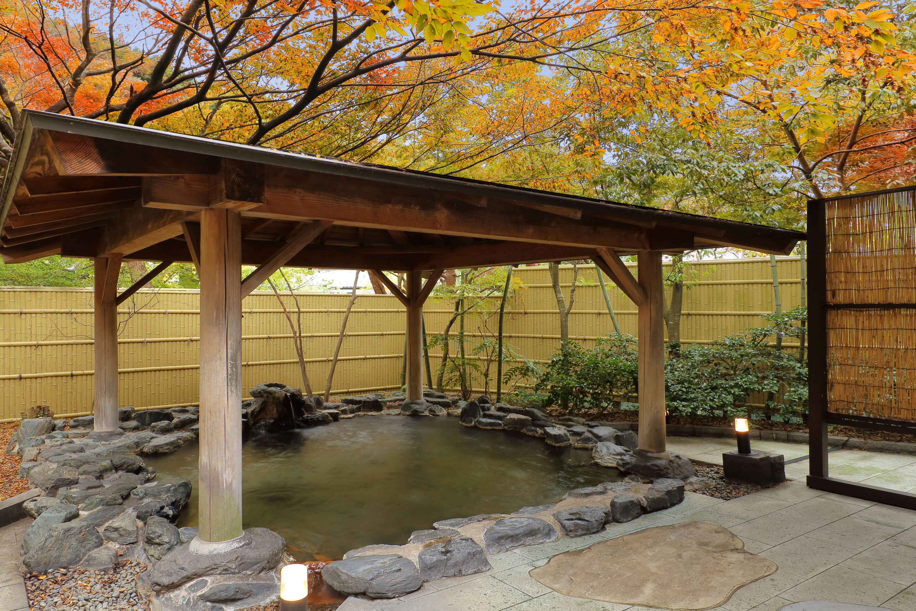 A traditional Japanese-style garden with a wooden pavilion, a koi pond, and a bamboo fence.
