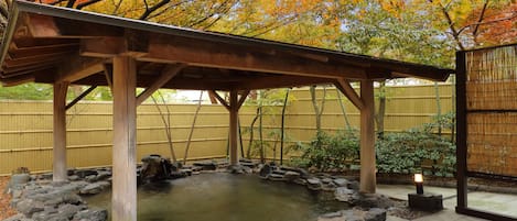 A traditional Japanese-style garden with a wooden pavilion, a koi pond, and a bamboo fence.