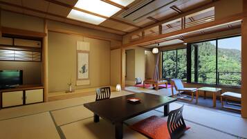 Quarto japonês tradicional com tatames, uma mesa baixa, cadeiras e uma televisão.