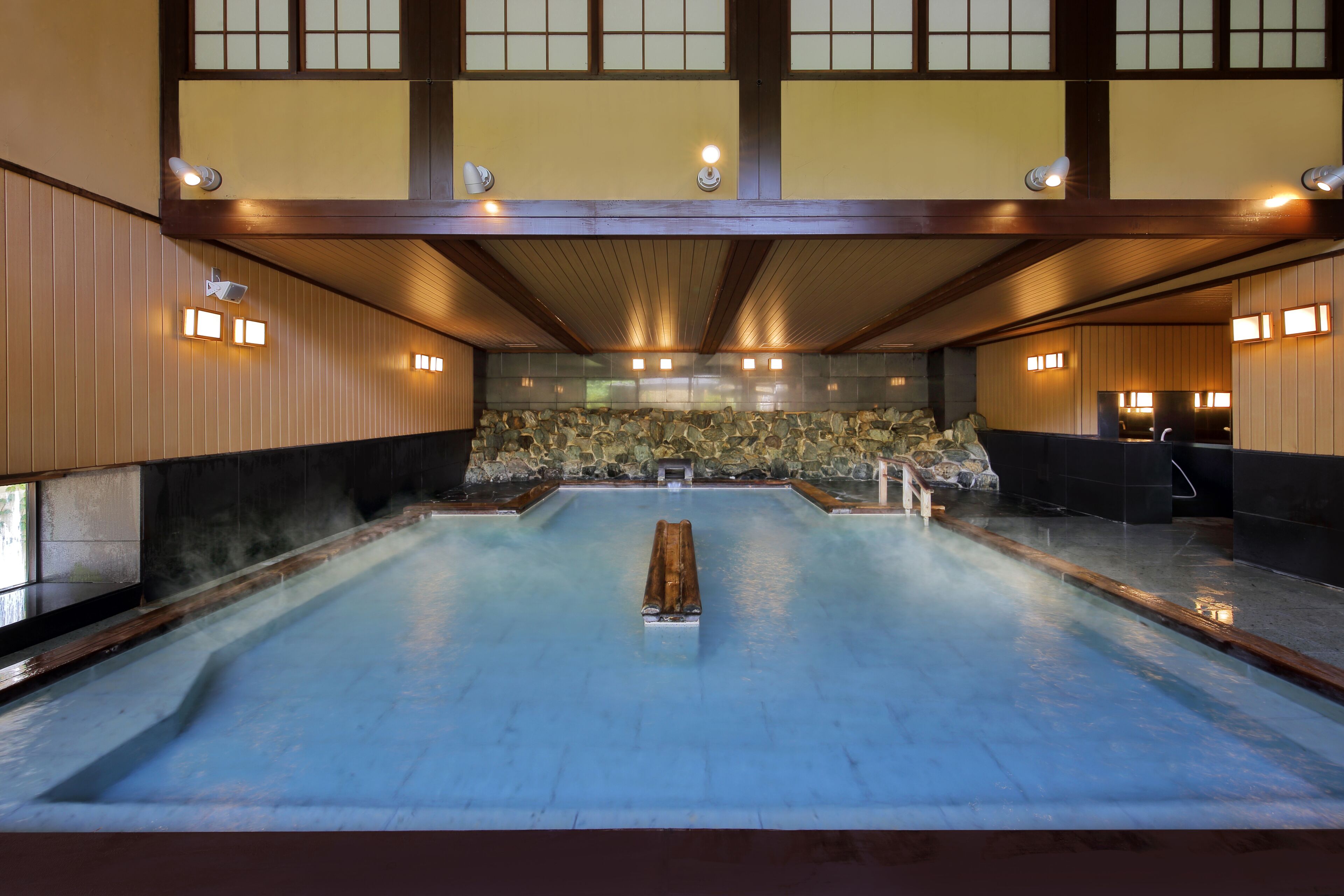 A traditional Japanese onsen with a stone wall backdrop, wooden beams, and tiled flooring.