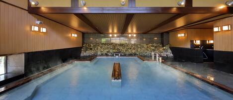 A traditional Japanese onsen with a stone wall backdrop, wooden beams, and tiled flooring.