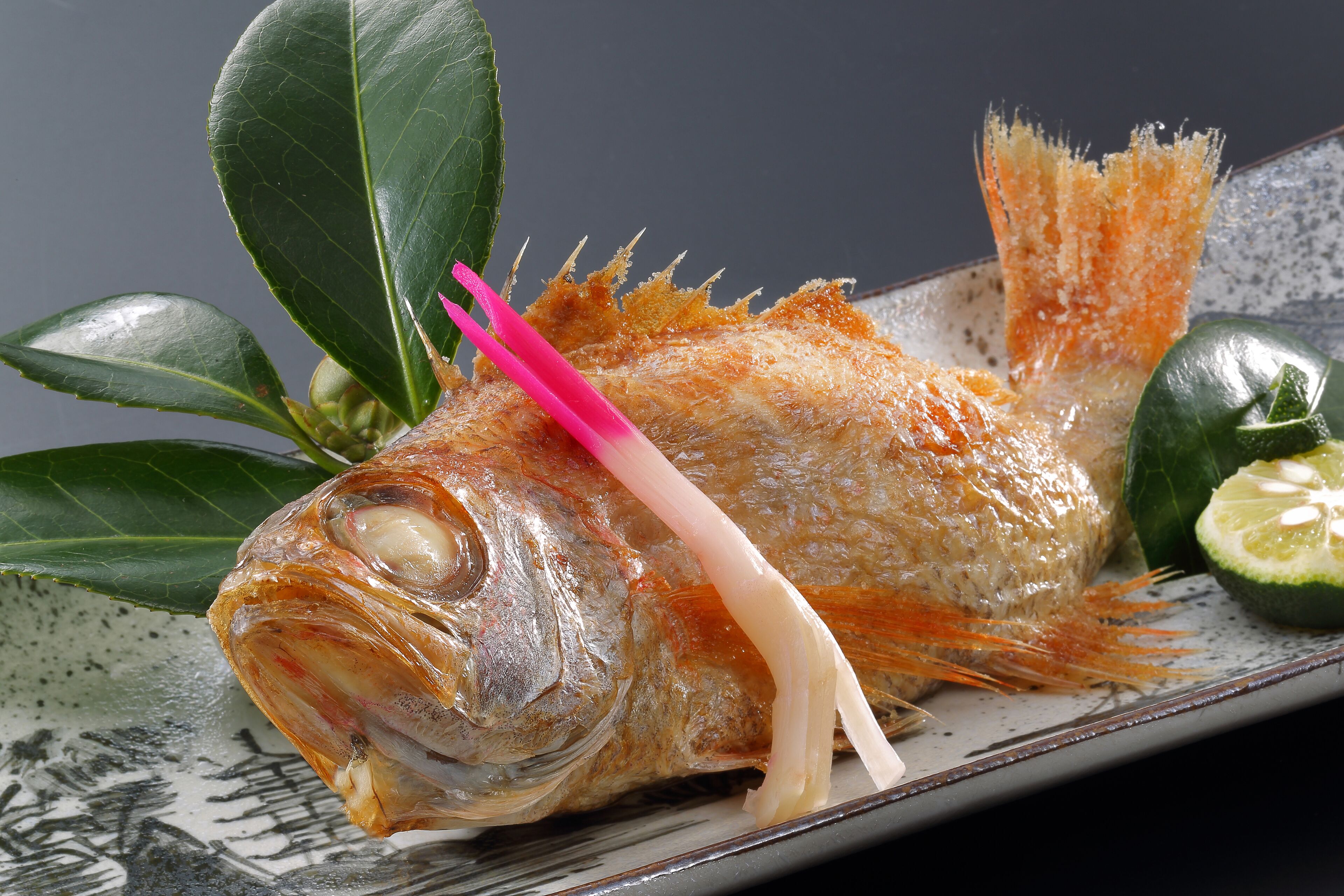 A whole fish with a pink garnish on a plate.