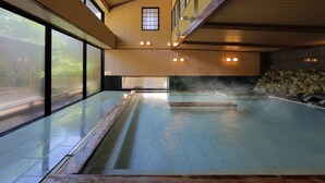 A traditional Japanese onsen with a wooden interior, a stone wall, and a view of the outside. - Tachibanaya (Tsuruoka)