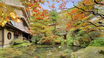 A traditional Japanese garden with a koi pond, stone lanterns, and a wooden building with a curved roof.