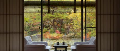 Una tradizionale stanza giapponese con pavimento in tatami, un tavolino con set da tè e vista su un giardino attraverso delle porte scorrevoli shoji.
