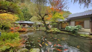 A traditional Japanese garden with koi fish in a pond, surrounded by autumn foliage and traditional buildings.