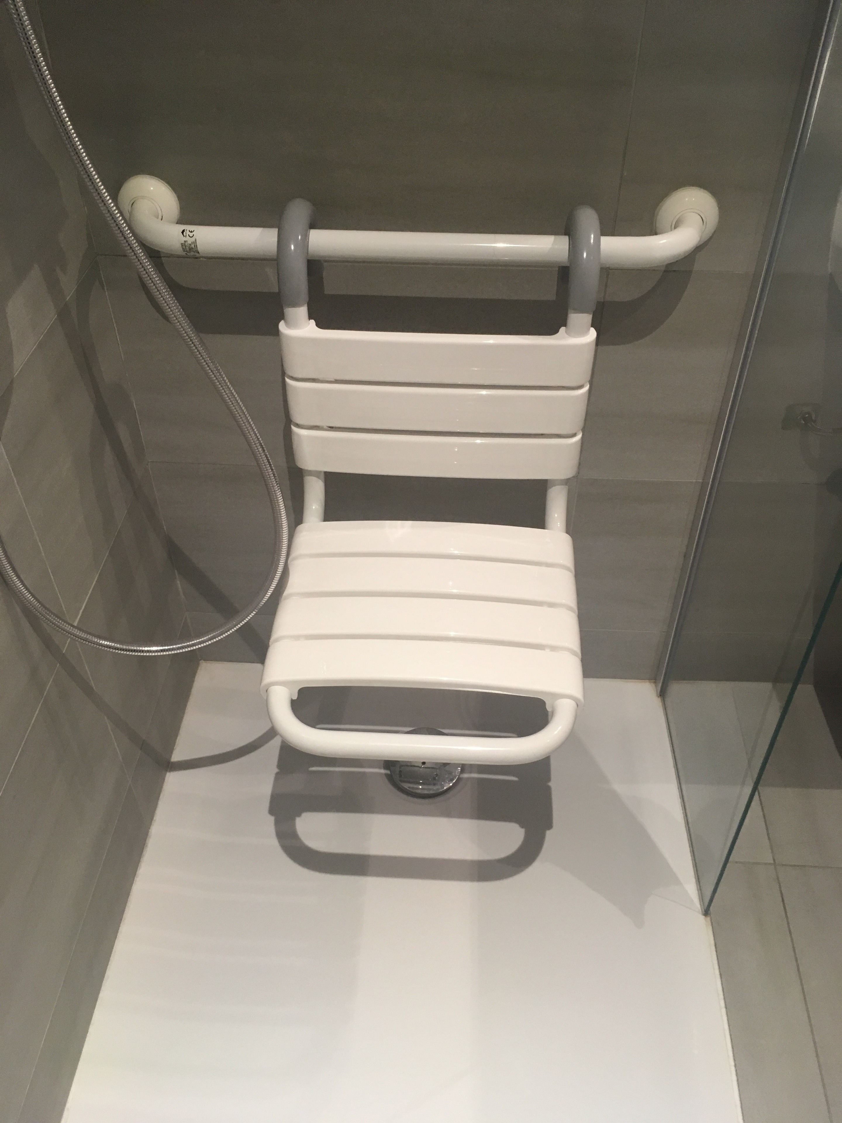 A shower area with a white grab bar and a handheld showerhead.