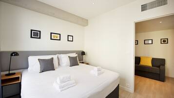 A hotel room with a large bed, a nightstand, a lamp, and a wall with framed pictures.