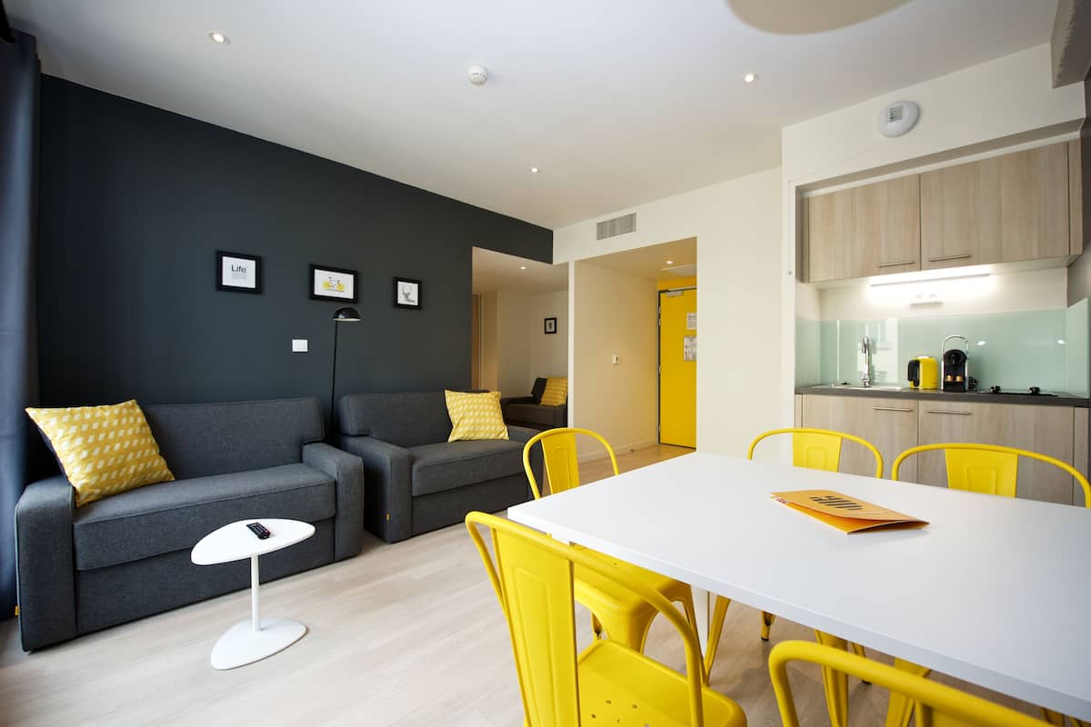 A modern living room with a grey sofa, yellow chairs, and a white table.
