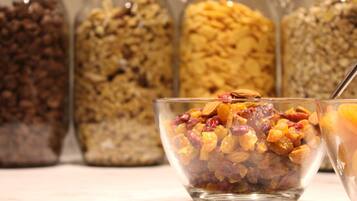 A bowl of mixed nuts and dried fruits in the foreground with jars of various grains and legumes in the background.