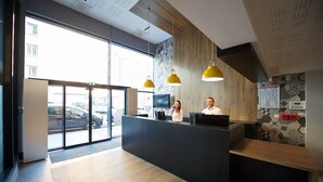 A reception area with a wooden reception desk, two staff members, and a large window overlooking the street. - Staycity Aparthotels, Lyon Rue Garibaldi (Lyon)