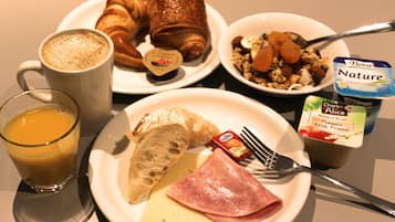 Prato de pequeno-almoço com croissants, fiambre, queijo e um copo de sumo de laranja.