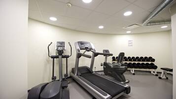 Une salle de sport équipée de tapis de course, de vélos elliptiques et d’un banc avec des haltères.