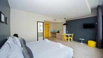 A hotel room with a bed, a desk, a chair, a small table, and a TV mounted on the wall.