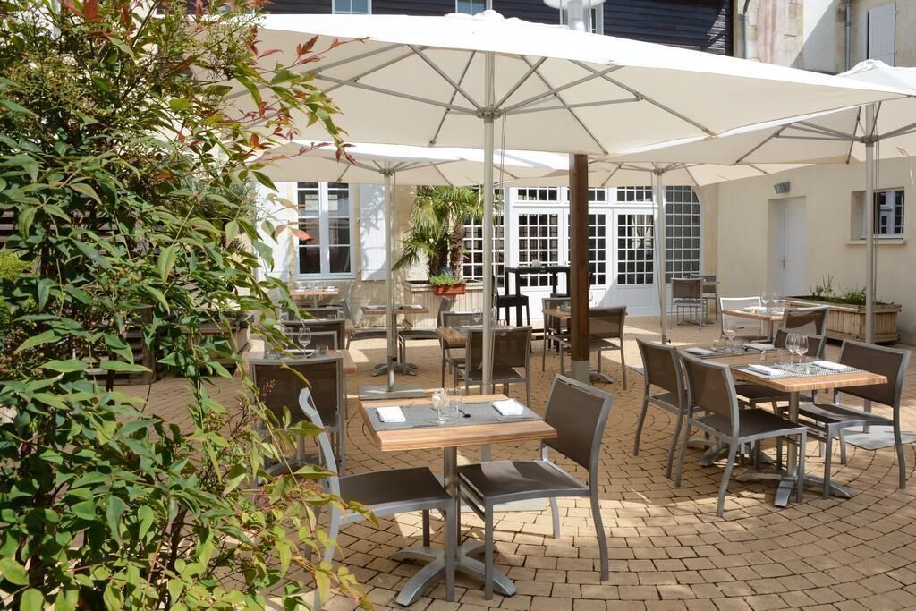 An outdoor patio with tables and chairs, umbrellas, and potted plants.