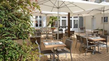 An outdoor patio with tables and chairs, umbrellas, and potted plants.