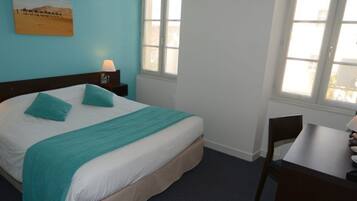 A bedroom with a bed, two bedside tables with lamps, a desk with a chair, and a window.