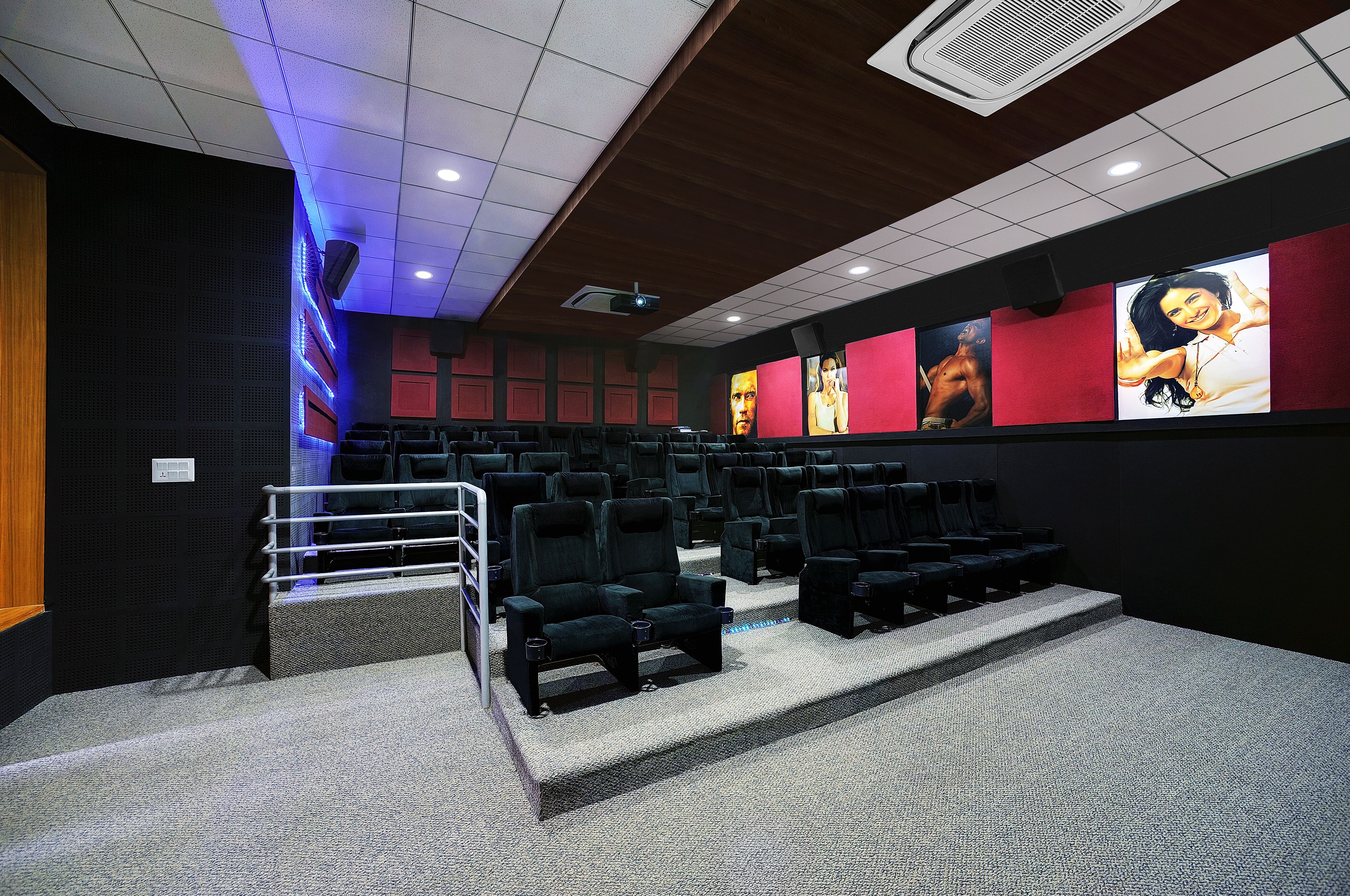 A movie theater with rows of seats, a projector, and a screen with movie posters.